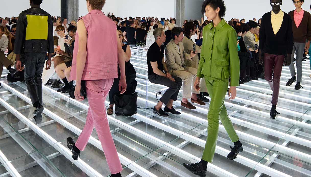 Modelli in look total color in pelle rosa e verde acido sfilano sul pavimento a griglia luminosa del Deposito della Fondazione Prada, SS27
