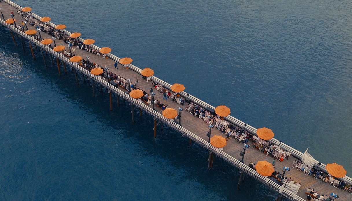 Vista aerea del Malibu Pier con file di ospiti seduti ai lati e ombrelloni arancioni sul Pacifico blu durante la sfilata Zegna Estate 2027