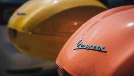 Dettaglio del logo Vespa su uno scooter Piaggio, immagine simbolo della mobilità urbana italiana e del settore delle due ruote.