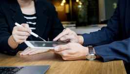 Clienti in banca consultano un tablet con un consulente, immagine simbolo del conto corrente gratuito per chi ha ISEE sotto 11.600 euro.