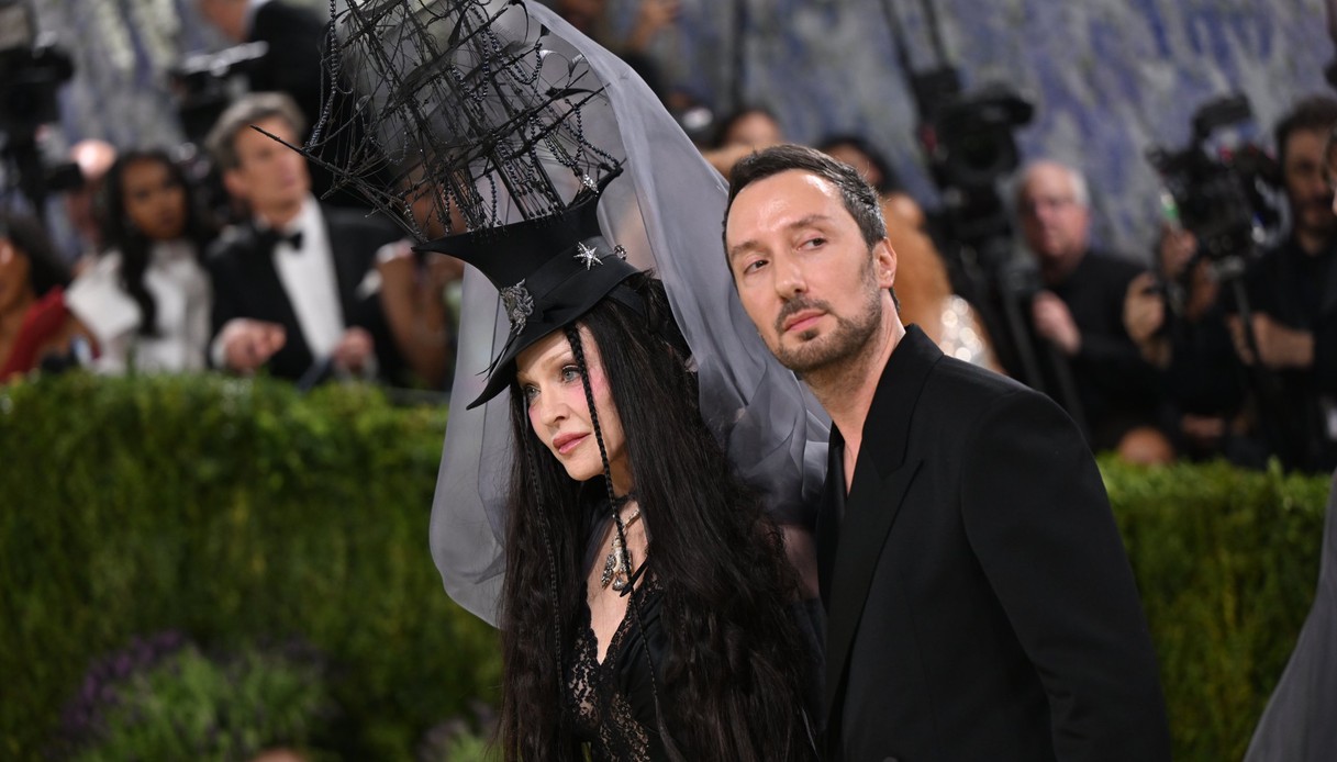 Anthony Vaccarello in completo nero accanto a Madonna, che indossa un cappello con un veliero scultoreo, velo grigio e abito di pizzo nero, sul red carpet del Met Gala 2026